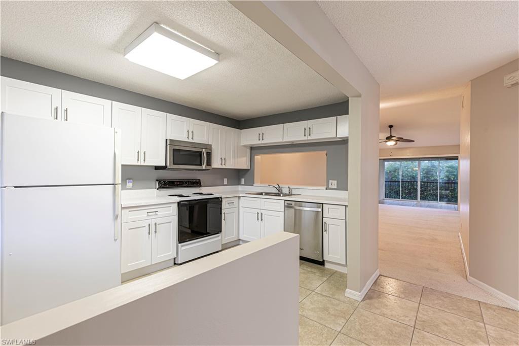 7761 Jewel Lane, Unit 202 Naples, FL 34109 - Photo 12 of 27 Kitchen with light tile patterned floors, a textured ceiling, white cabinets, and stainless steel appliances