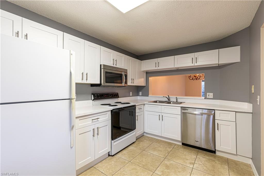 7761 Jewel Lane, Unit 202 Naples, FL 34109 - Photo 14 of 27 Kitchen with appliances with stainless steel finishes, sink, white cabinetry, light tile patterned flooring, and a textured ceiling