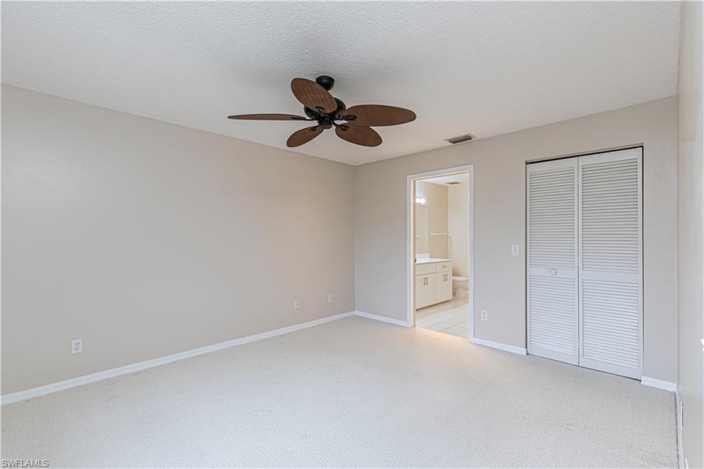 7761 Jewel Lane, Unit 202 Naples, FL 34109 - Photo 16 of 27 Unfurnished bedroom featuring a textured ceiling, a closet, light colored carpet, ceiling fan, and connected bathroom