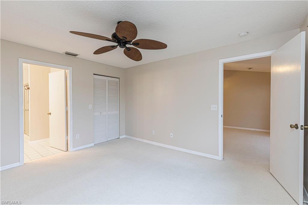 7761 Jewel Lane, Unit 202 Naples, FL 34109 - Photo 19 of 27 Unfurnished bedroom with a textured ceiling, a closet, ceiling fan, light colored carpet, and ensuite bathroom