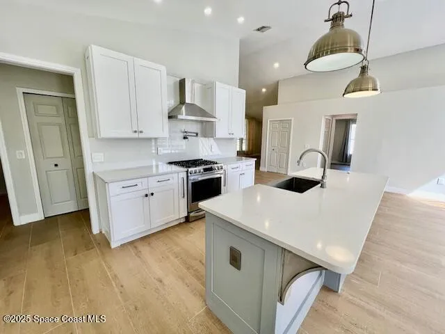 a kitchen with stainless steel appliances a stove a sink a refrigerator and white cabinets with wooden floor