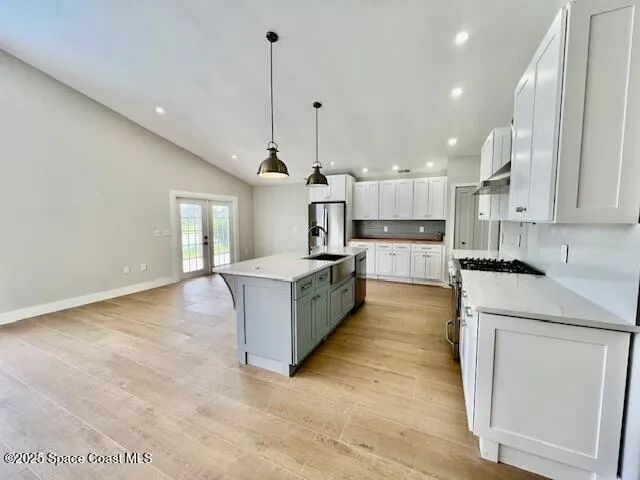 a large kitchen with stainless steel appliances kitchen island a large counter top a stove a chimney a sink and a refrigerator
