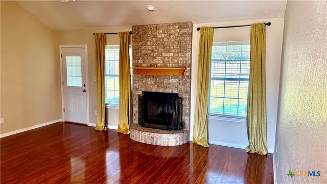 an empty room with wooden floor a fireplace and windows