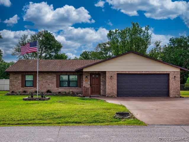 a view of a house with a yard plants and a large tree