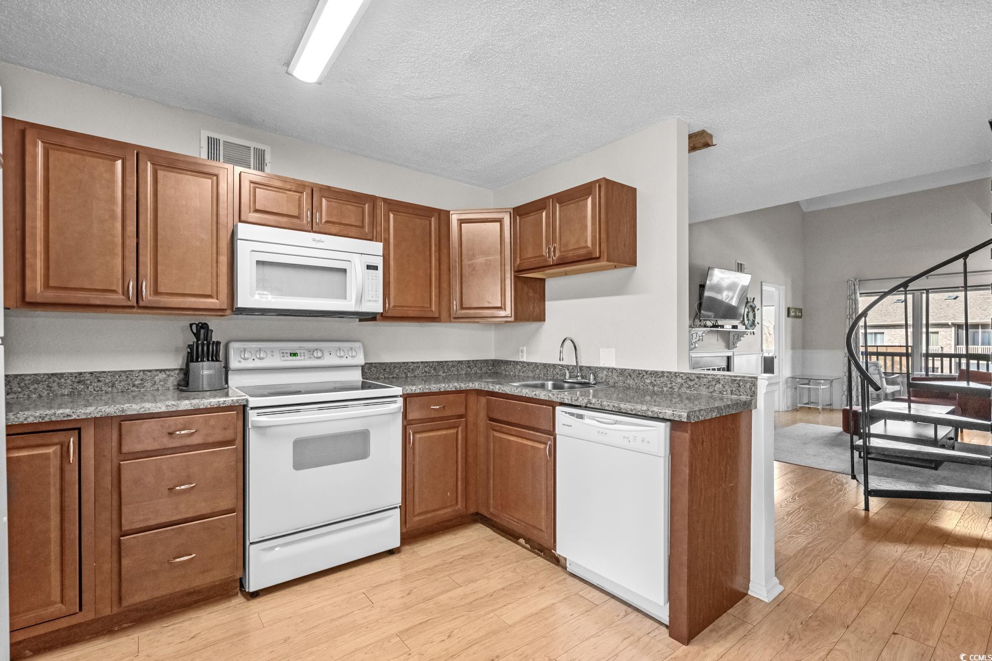 1356 Glenns Bay Road, Unit 203D Surfside Beach, SC 29575 - Photo 11 of 38 Kitchen featuring white appliances, brown cabinetry, light wood-style floors, a textured ceiling, and dark stone countertops