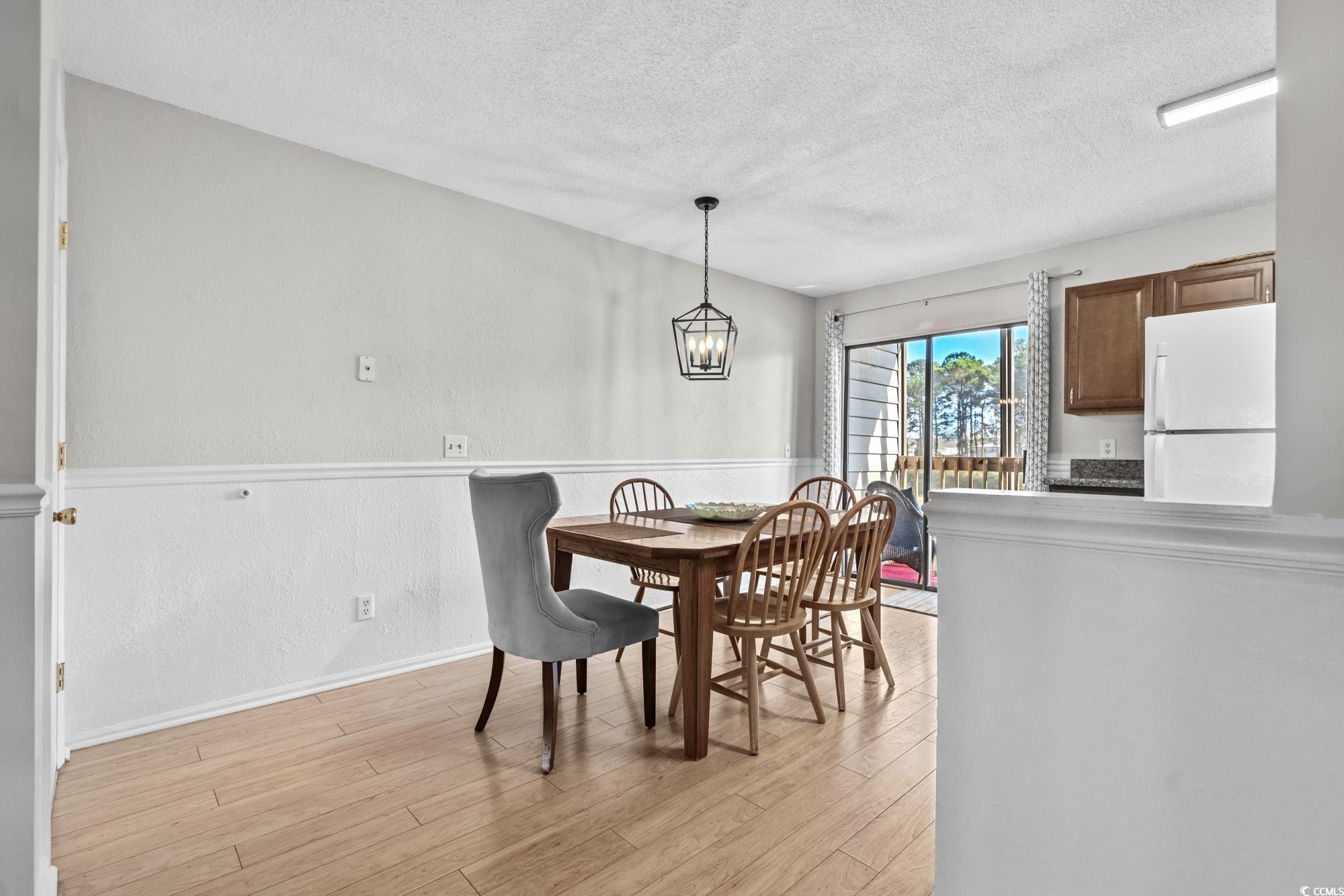 1356 Glenns Bay Road, Unit 203D Surfside Beach, SC 29575 - Photo 8 of 38 Dining area featuring a textured ceiling, a textured wall, light wood-style flooring, and a chandelier