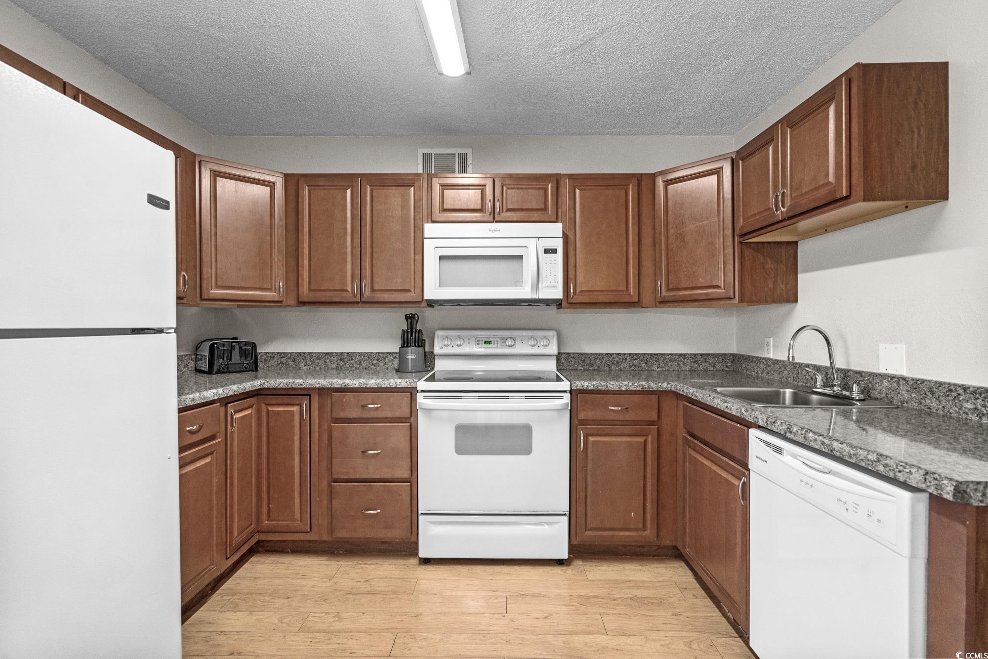 1356 Glenns Bay Road, Unit 203D Surfside Beach, SC 29575 - Photo 10 of 38 Kitchen with white appliances, brown cabinetry, light wood-type flooring, and a textured ceiling