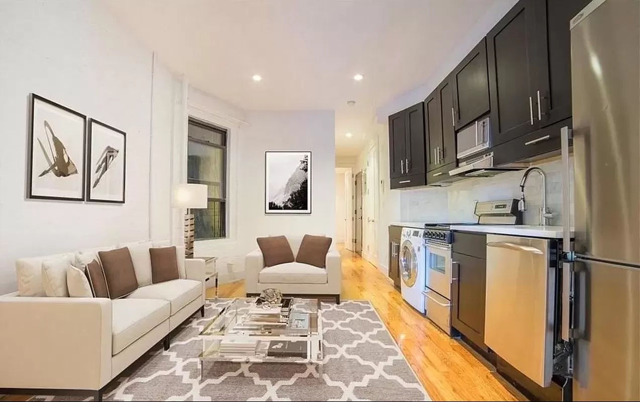 a living room with stainless steel appliances furniture a rug and a kitchen view
