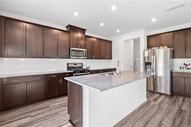 a kitchen with stainless steel appliances granite countertop a refrigerator a sink dishwasher a stove with wooden cabinets and floor