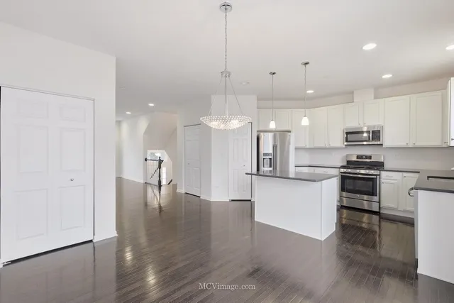 a kitchen with stainless steel appliances granite countertop a refrigerator a sink dishwasher a stove and white cabinets with wooden floor