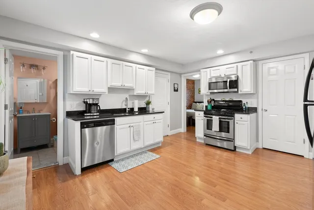 a kitchen with granite countertop a refrigerator a sink a stove top oven and white cabinets