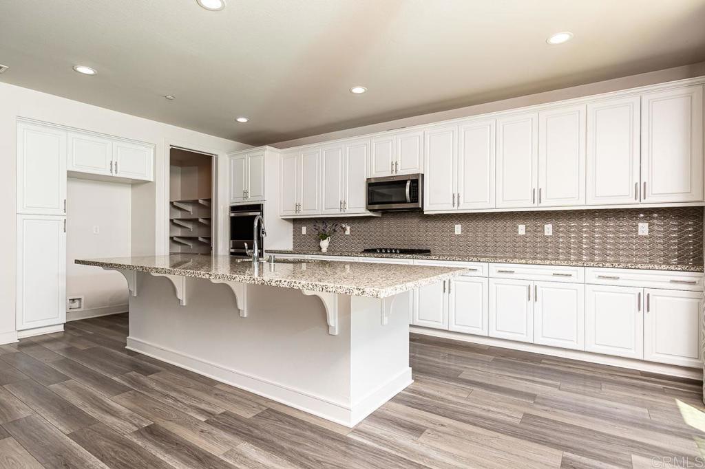 1281 Palomar Circle Escondido, CA 92027 - Photo 3 of 31 a large white kitchen with granite countertop a stove a sink a refrigerator and white cabinets with wooden floor