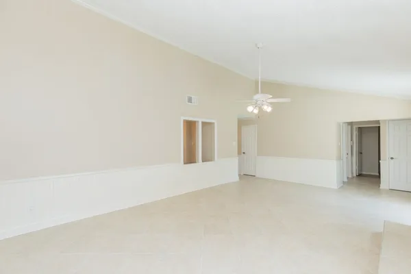 an empty room with chandelier fan and windows