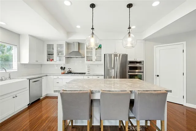 a kitchen with stainless steel appliances granite countertop a sink a stove a refrigerator and island with wooden floor