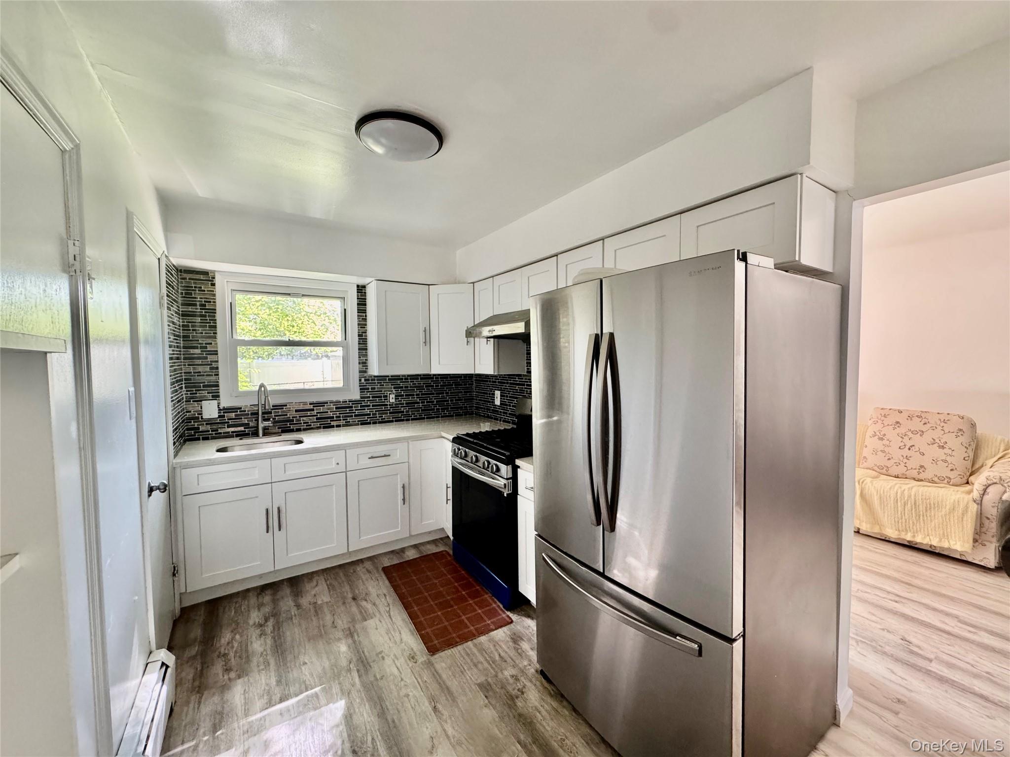 17 North Aspen Road Middletown, NY 10940 - Photo 6 of 12 Kitchen with appliances with stainless steel finishes, tasteful backsplash, white cabinetry, light wood-style floors, and baseboard heating