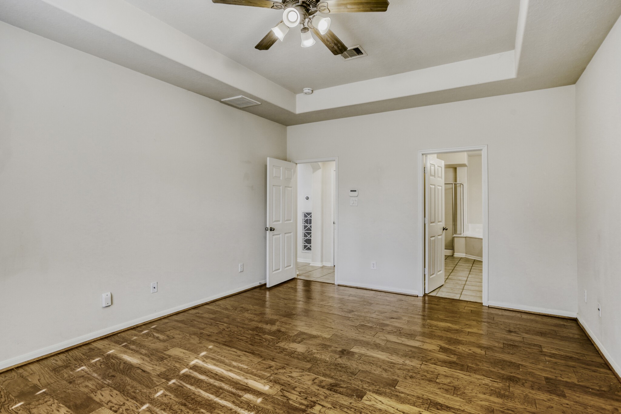 19303 Valiant Woods Drive Spring, TX 77379 - Photo 16 of 27 This spacious master bedroom features elegant hardwood floors, a stylish tray ceiling with a fan, and an en-suite bathroom, creating a luxurious retreat.