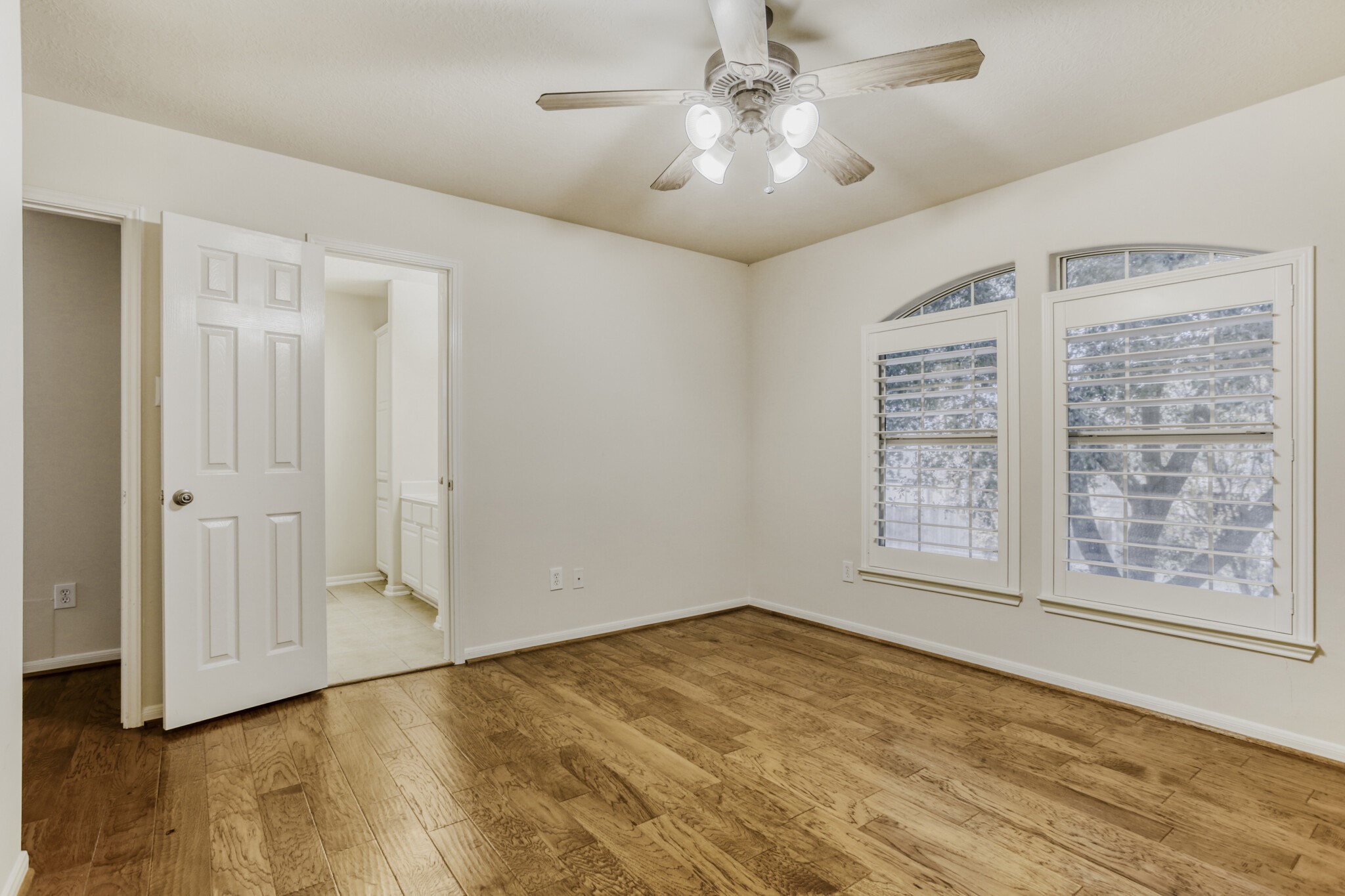 19303 Valiant Woods Drive Spring, TX 77379 - Photo 19 of 27 This inviting secondary bedroom features elegant hardwood floors, abundant natural light through stylish arched windows, and easy access to a convenient ensuite bathroom.