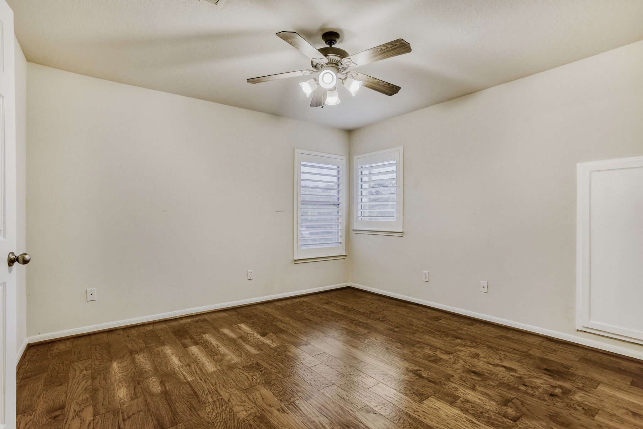 19303 Valiant Woods Drive Spring, TX 77379 - Photo 21 of 27 This room features warm wooden flooring, neutral walls, a ceiling fan with lights, and two windows with shutters, offering a cozy and versatile space.