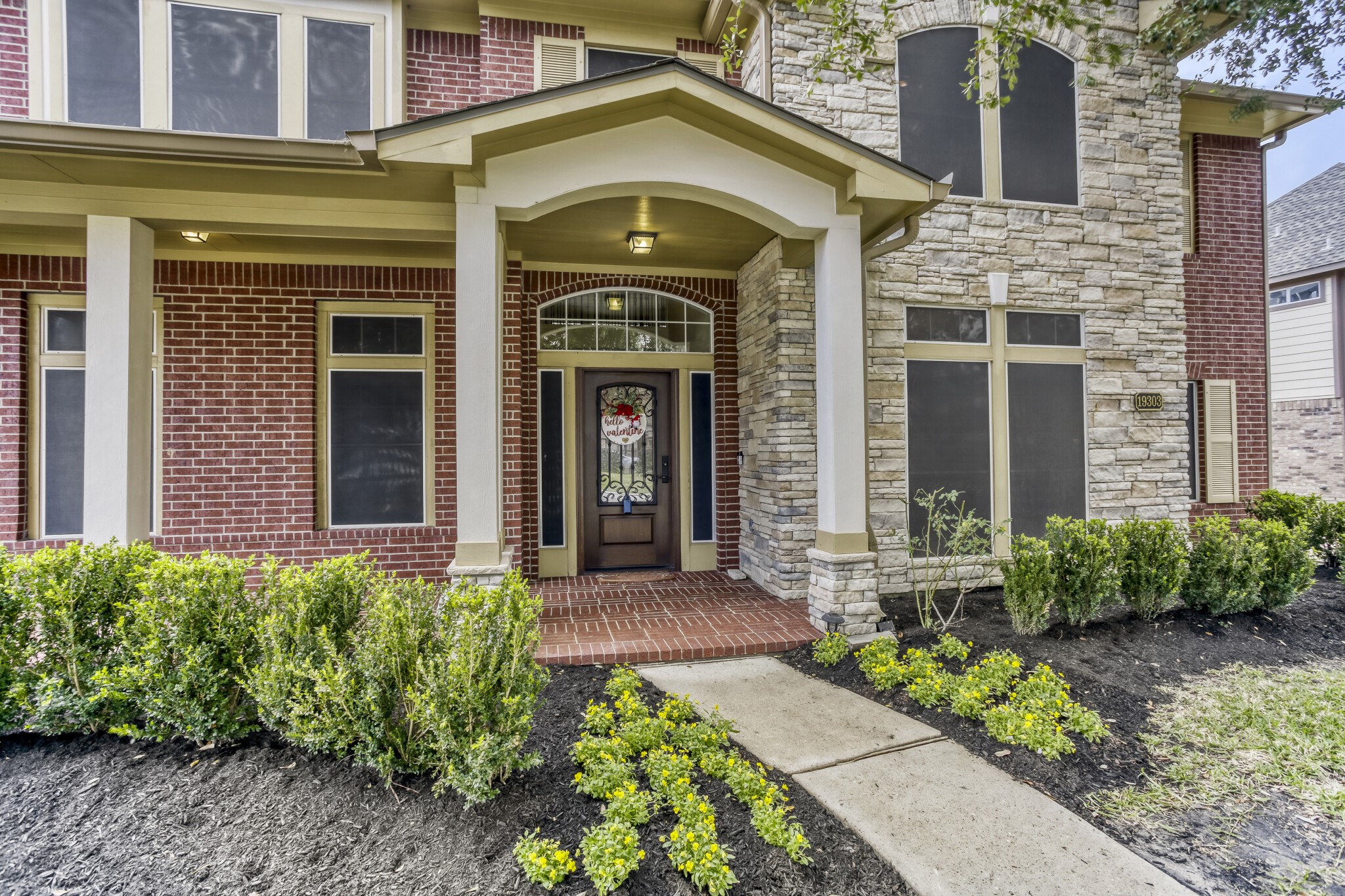 19303 Valiant Woods Drive Spring, TX 77379 - Photo 3 of 27 Enjoy the charm of this home's inviting front facade, featuring elegant brick and stonework, complemented by lush landscaping and a welcoming covered entryway.