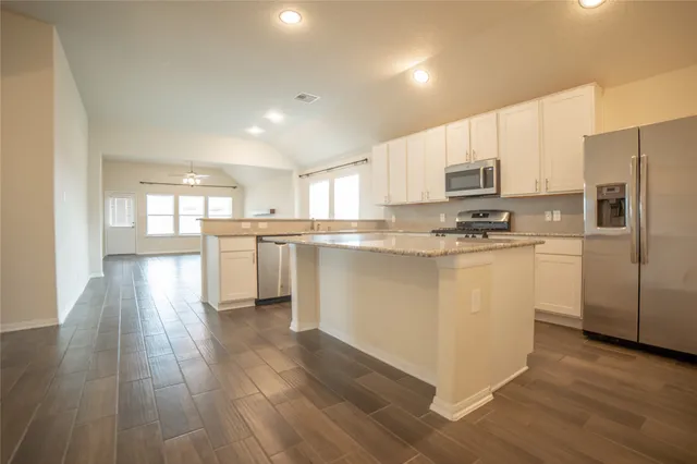 a kitchen with stainless steel appliances granite countertop a refrigerator a stove top oven a sink and a island with wooden floor