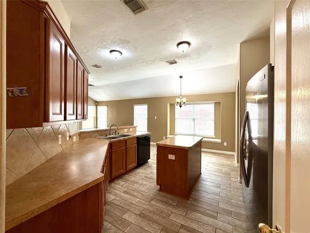 a large kitchen with stainless steel appliances granite countertop a refrigerator a sink dishwasher a stove and a dining table with wooden floor