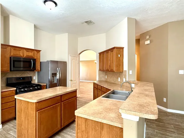 a kitchen with stainless steel appliances kitchen island granite countertop a sink a stove and a wooden floors