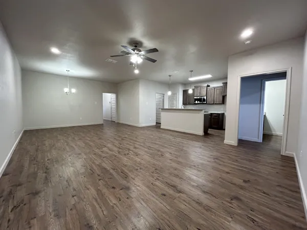 an empty room with wooden floor ceiling fan and kitchen view