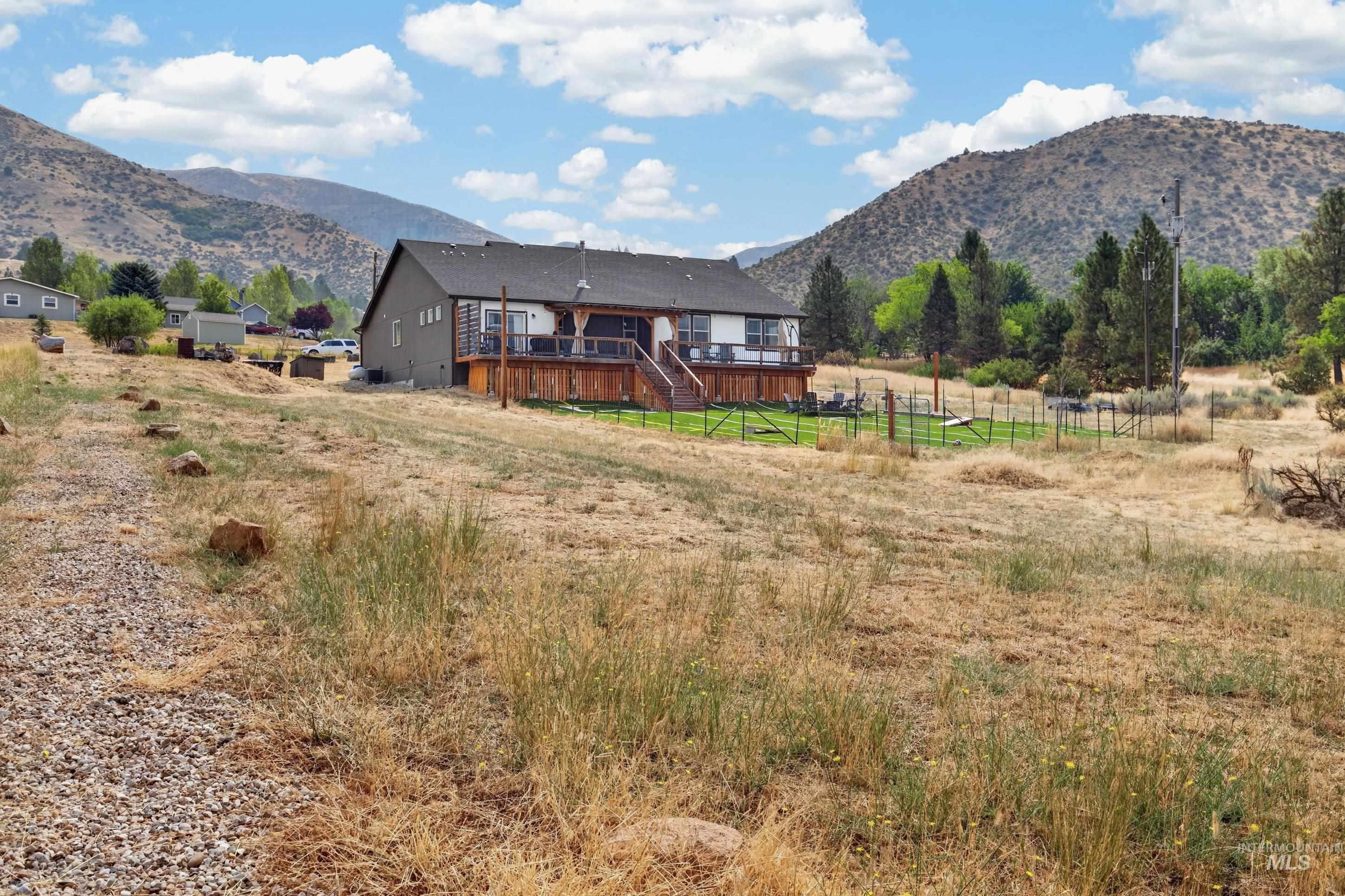 132 Mores Creek Rim Road Boise, ID 83716 - Photo 42 of 44 Rear exterior featuring a multi-level deck with wooden railings, a partially fenced yard, and a distant mountainous backdrop