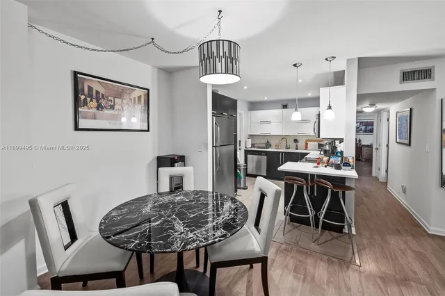 a kitchen with stainless steel appliances a refrigerator a sink a stove a dining table and chairs with wooden floor