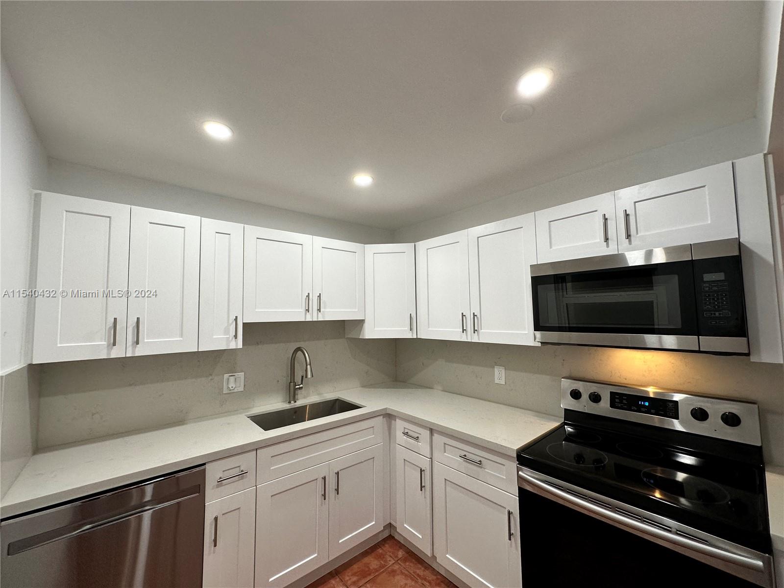7785 Southwest 86th Street, Unit E116 Miami, FL 33143 - Photo 7 of 27 a kitchen with stainless steel appliances a sink a stove cabinets and a microwave