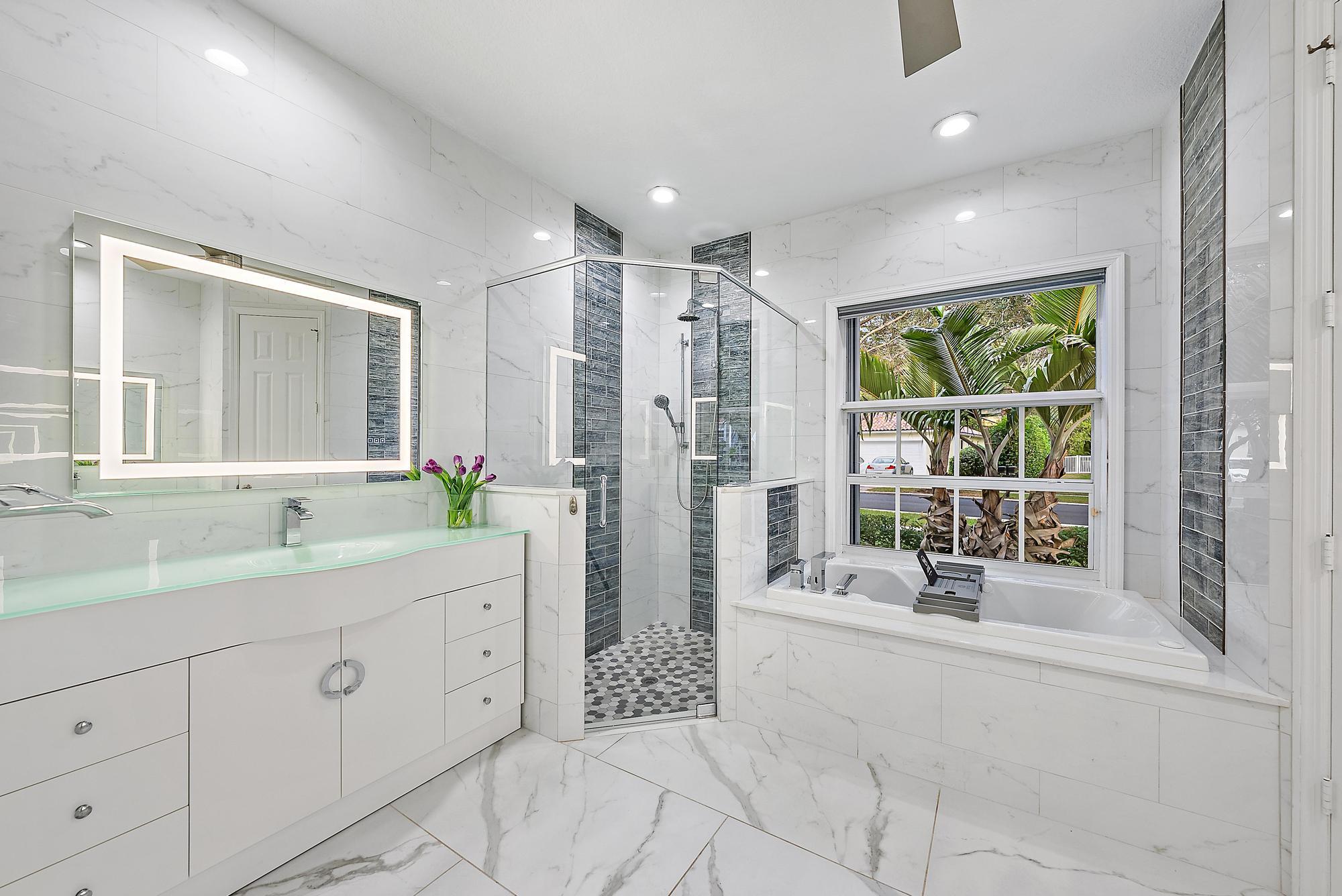9790 Southeast Crape Myrtle Court Hobe Sound, FL 33455 - Photo 18 of 74 a spacious bathroom with a double vanity sink a mirror a bathtub and next to a window