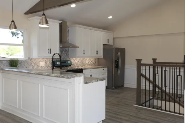 a kitchen with stainless steel appliances granite countertop a refrigerator a sink dishwasher a stove and white cabinets with wooden floor