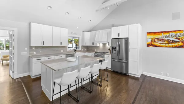 a kitchen with stainless steel appliances granite countertop a refrigerator a stove a sink and white cabinets with wooden floor