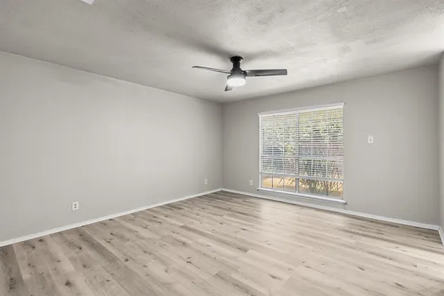 an empty room with wooden floor ceiling fan and windows