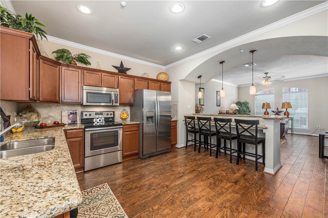 1198 Jones-Butler Road, Unit 2201 College Station, TX 77840 - Photo 5 of 8 a kitchen with stainless steel appliances kitchen island granite countertop a stove top oven a sink dishwasher a dining table and chairs with wooden floor