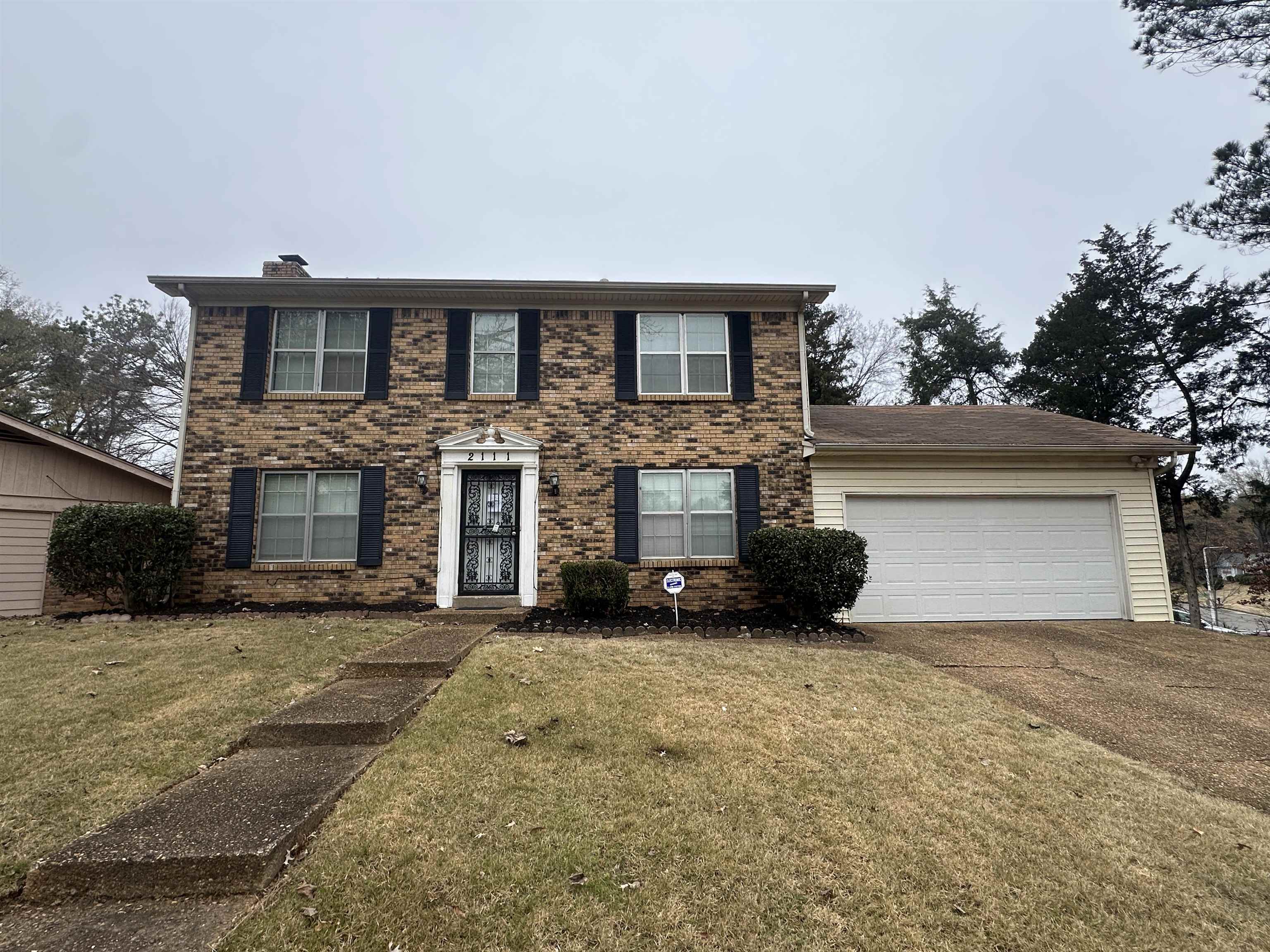 Colonial-style house with brick siding, driveway, an attached garage, and a front lawn