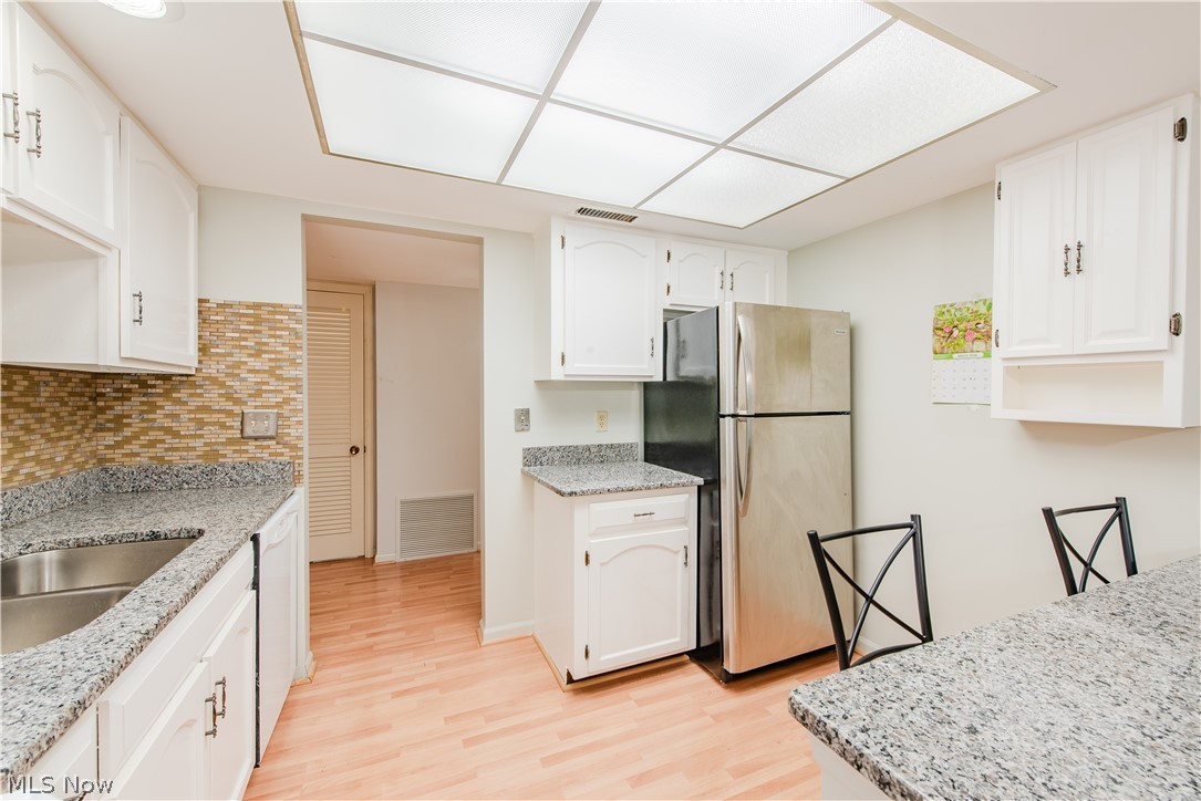 22701 Center Ridge Road, Unit 207 Rocky River, OH 44116 - Photo 9 of 26 Kitchen featuring freestanding refrigerator, light wood finished floors, light stone countertops, white cabinets, and dishwasher