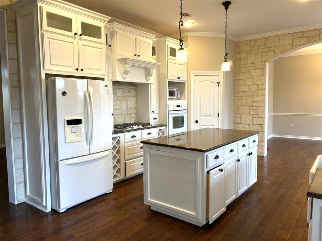 1170 Brazos Loop Gholson, TX 76705 - Photo 11 of 37 Kitchen featuring an island with a granite countertop, white cabinetry with black hardware, wood-finish flooring, and a stone accent wall