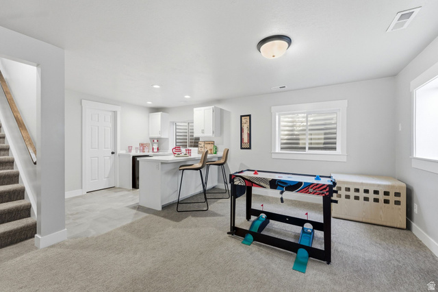 1405 Vintry Lane Murray, UT 84121 - Photo 26 of 44 Lower-level living area featuring neutral carpet flooring, a white kitchen with a peninsula, light gray wall paint, and windows with white trim