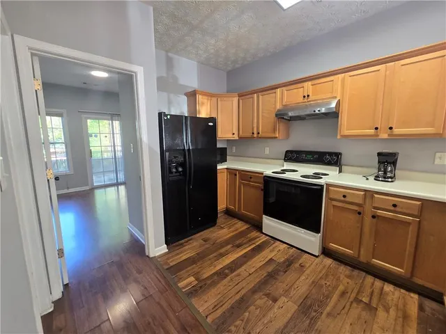 a kitchen with stainless steel appliances granite countertop a refrigerator a sink dishwasher a stove and white countertops with wooden floor