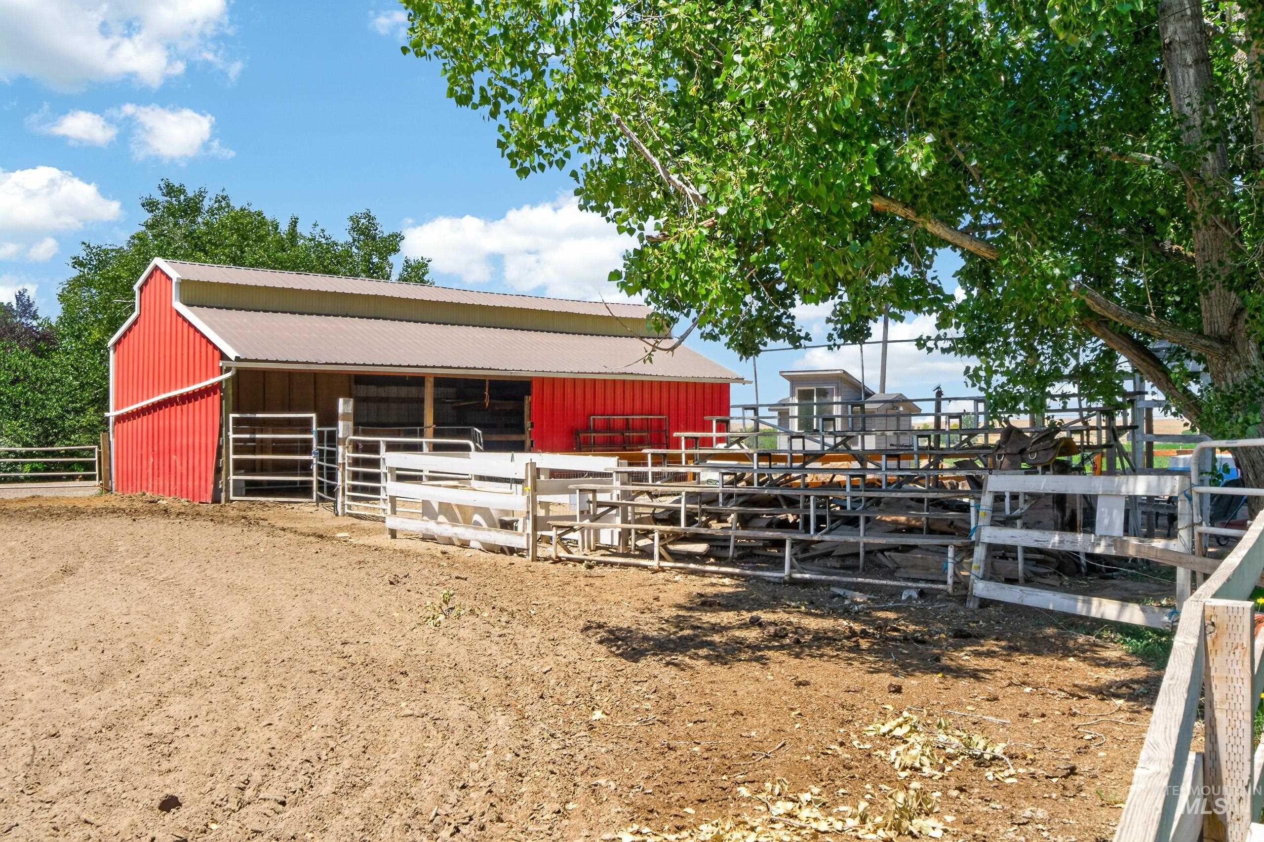 9696 Gloria Road Middleton, ID 83644 - Photo 40 of 50 Red barn structure with a metal roof, featuring multiple fenced enclosures and a large, open dirt ground area