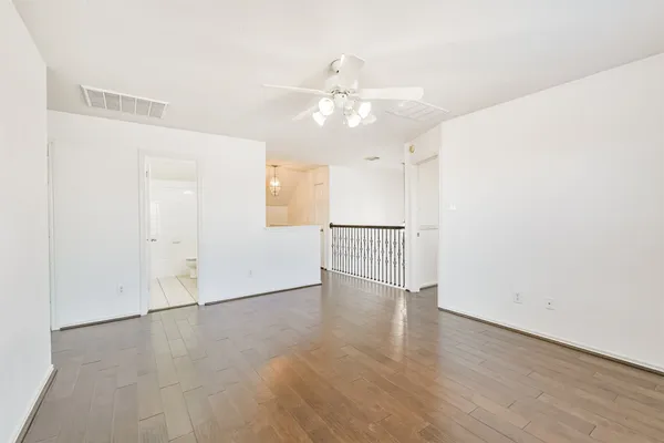 an empty room with wooden floor chandelier fan and windows