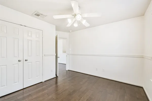 an empty room with wooden floor chandelier fan and windows