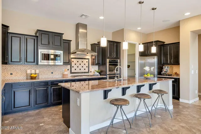 a kitchen with stainless steel appliances kitchen island granite countertop a table chairs sink refrigerator and microwave