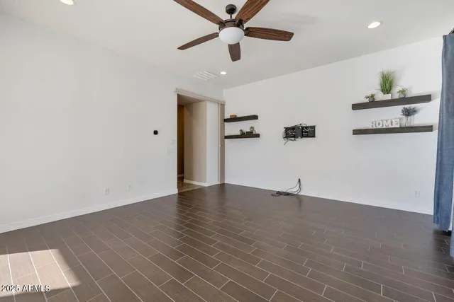 a view of an empty room with wooden floor and a ceiling fan