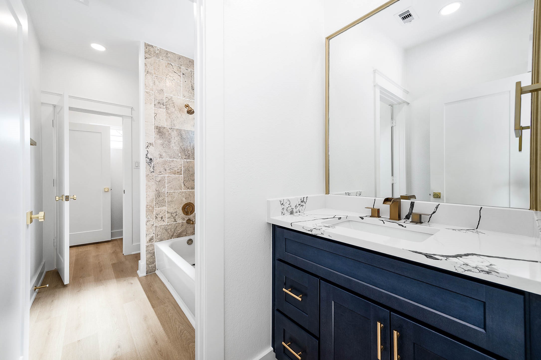 8602 Hoffman Street Houston, TX 77016 - Photo 24 of 30 Adjoining bath featuring a beautifully tiled tub/shower surround and an ash-blue vanity that continues the home’s cohesive color palette, paired with quartz counters and brushed gold accents for a polished finish.