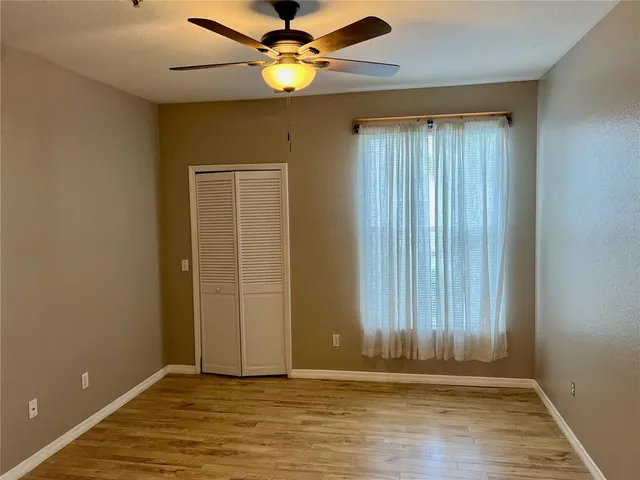 an empty room with wooden floor fan and windows