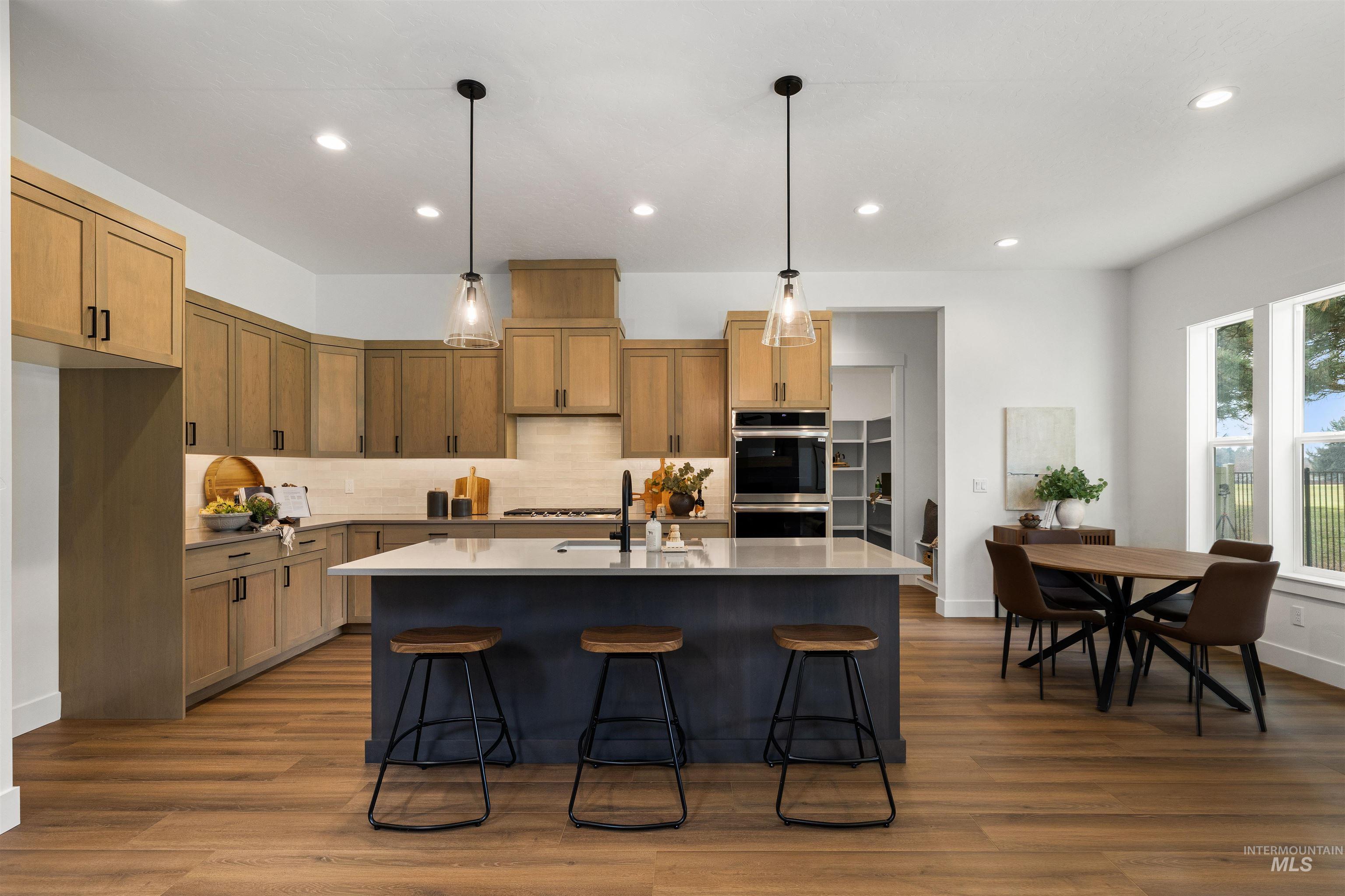 611 North Hiltonhead Way Eagle, ID 83616 - Photo 11 of 38 Kitchen featuring hanging light fixtures, an island with sink, a kitchen breakfast bar, dark wood-style floors, and appliances with stainless steel finishes