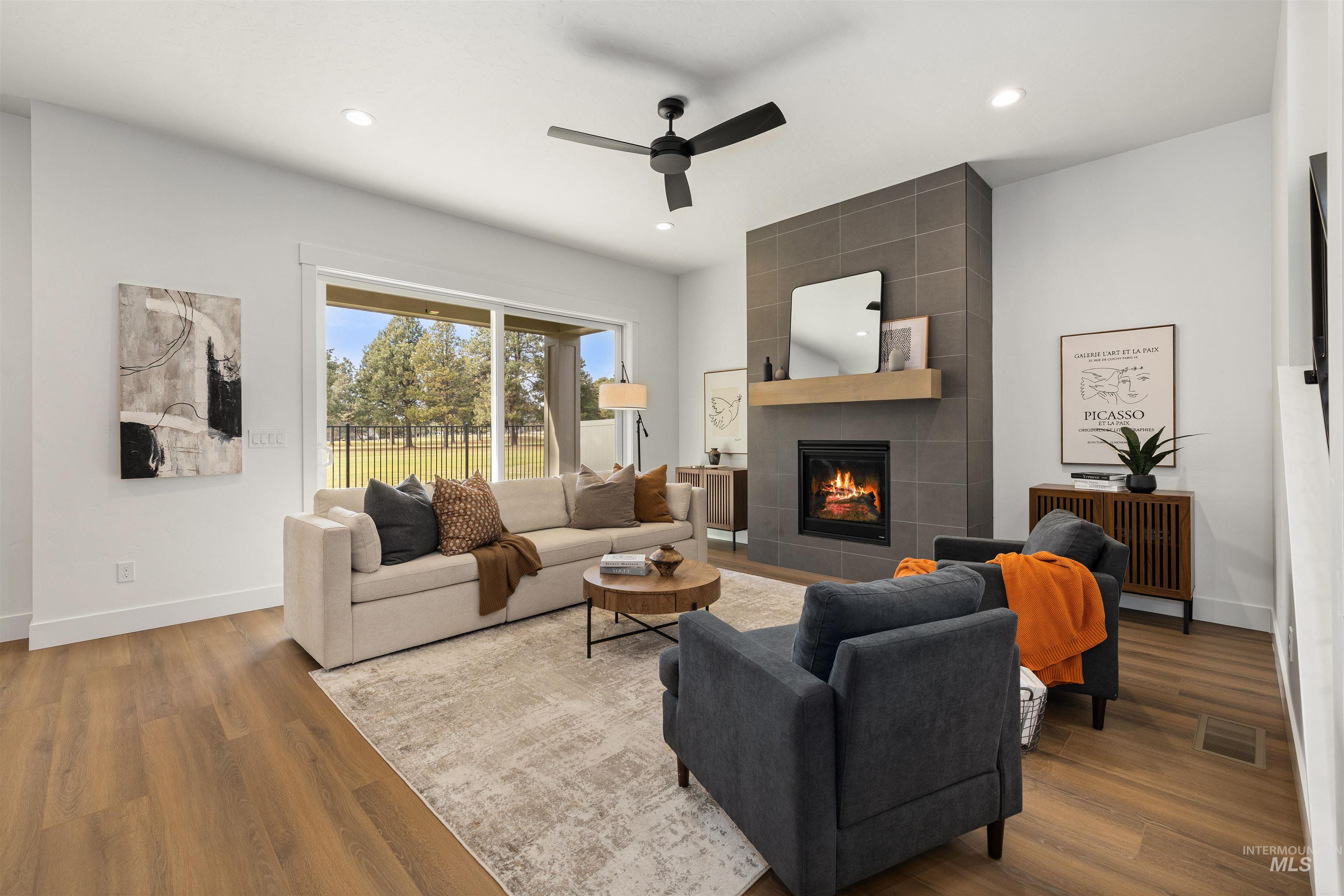 611 North Hiltonhead Way Eagle, ID 83616 - Photo 7 of 37 Living room featuring a tiled fireplace, wood finished floors, ceiling fan, recessed lighting, and radiator. Photo Similar.