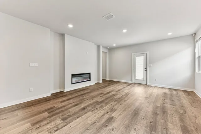 an empty room with wooden floor fireplace and windows